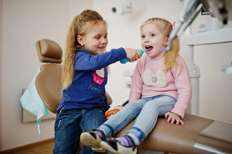 Dos niñas jugando a cepillarse los dientes en el sillón del dentista